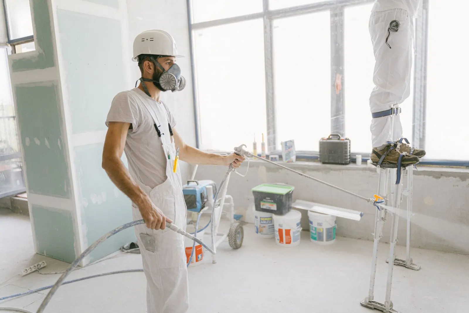 A painter in protective gear spraying an interior wall with a fine, even coat
