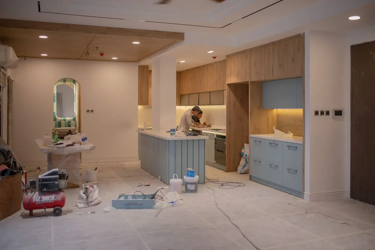 A kitchen part-way through a refinish, with the island and cabinet runs masked off and tools on the floor