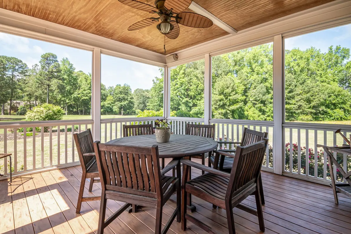 A covered wooden deck with a painted railing, a table and chairs looking out over open ground