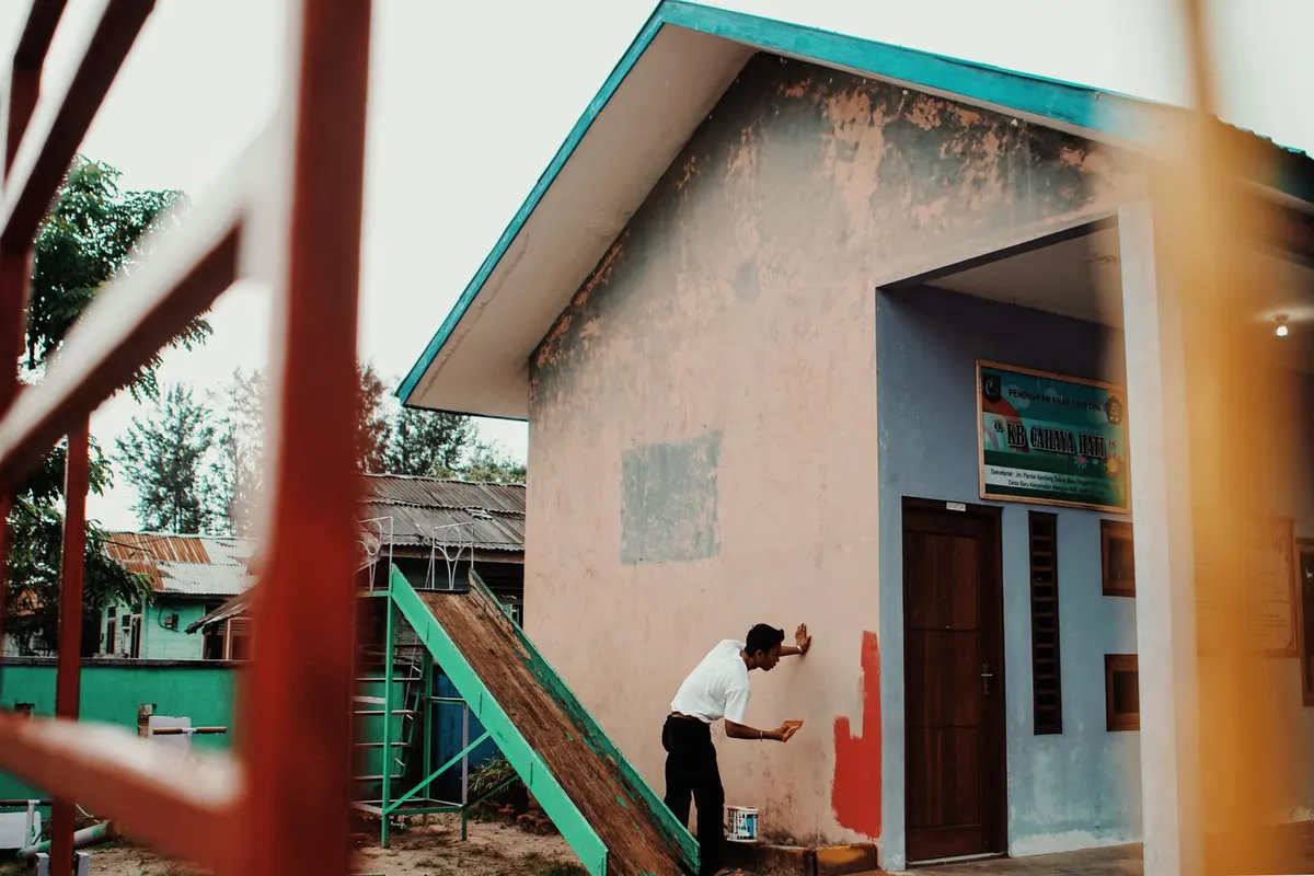 A painter using a long-handled roller to coat the exterior wall of a single-story house