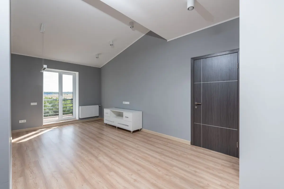 An empty apartment room with freshly painted walls and a bare wood floor, ready for the next tenant