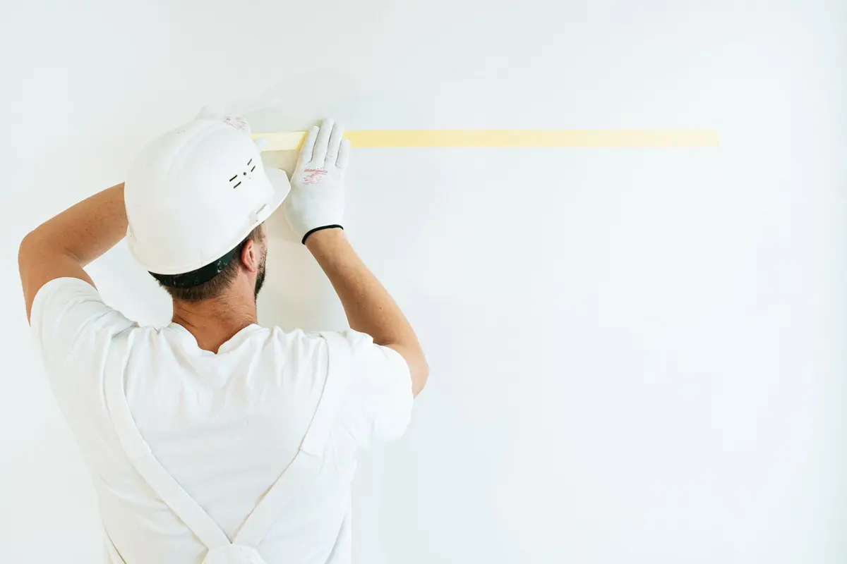 A worker in a hard hat masking a wall off with tape before any paint is opened