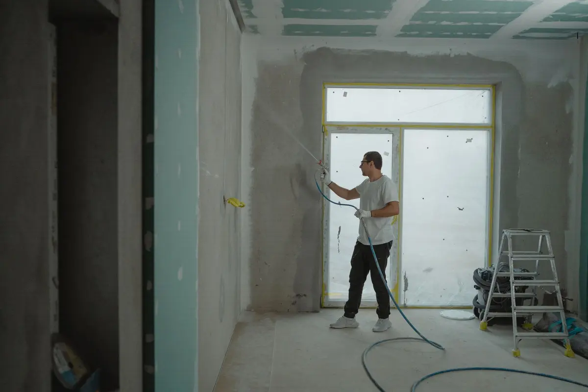 A worker spraying texture onto an interior wall with a hose-fed spray rig
