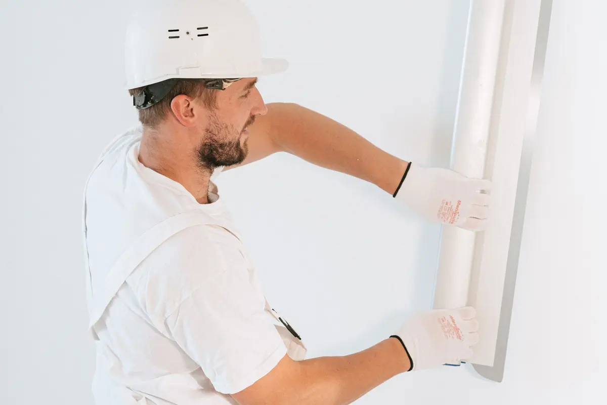 A worker in a hard hat and gloves working on a section of interior wall